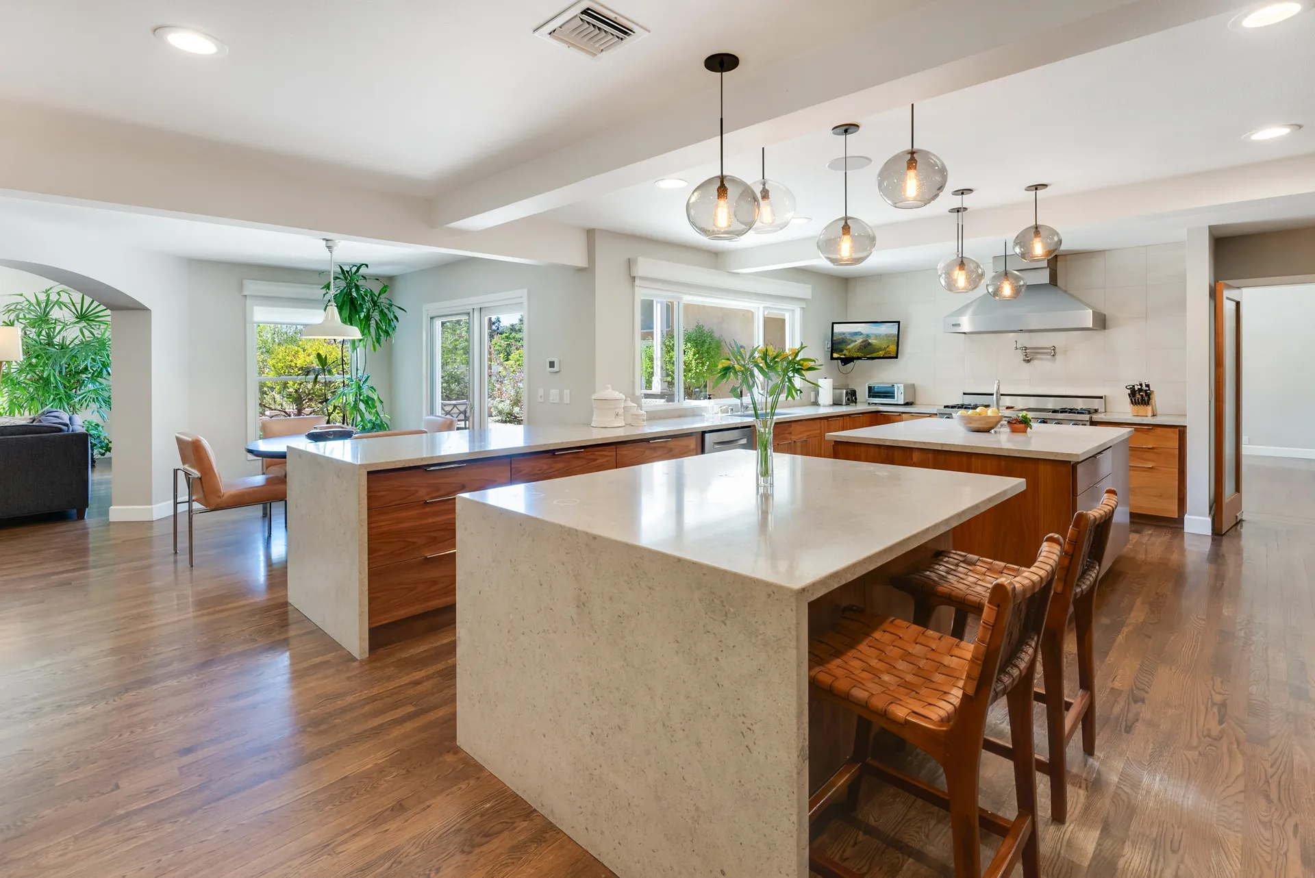 Kitchen with large island, wood cabinets, pendant lights, and plants with natural light